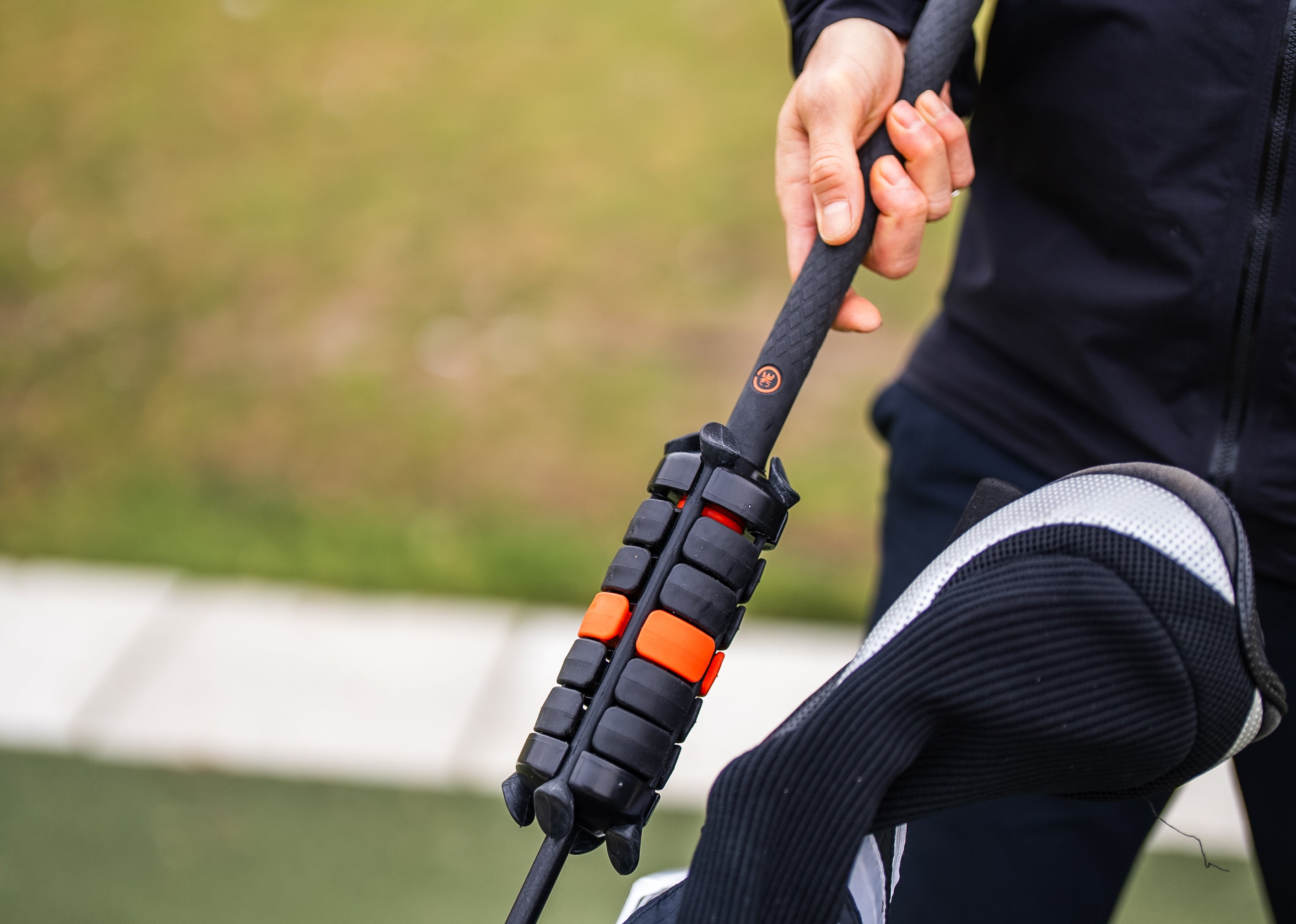 ONE Club swing trainer held by a golfer beside a golf bag, weighted cylinder loaded with black 65g and orange 135g discs